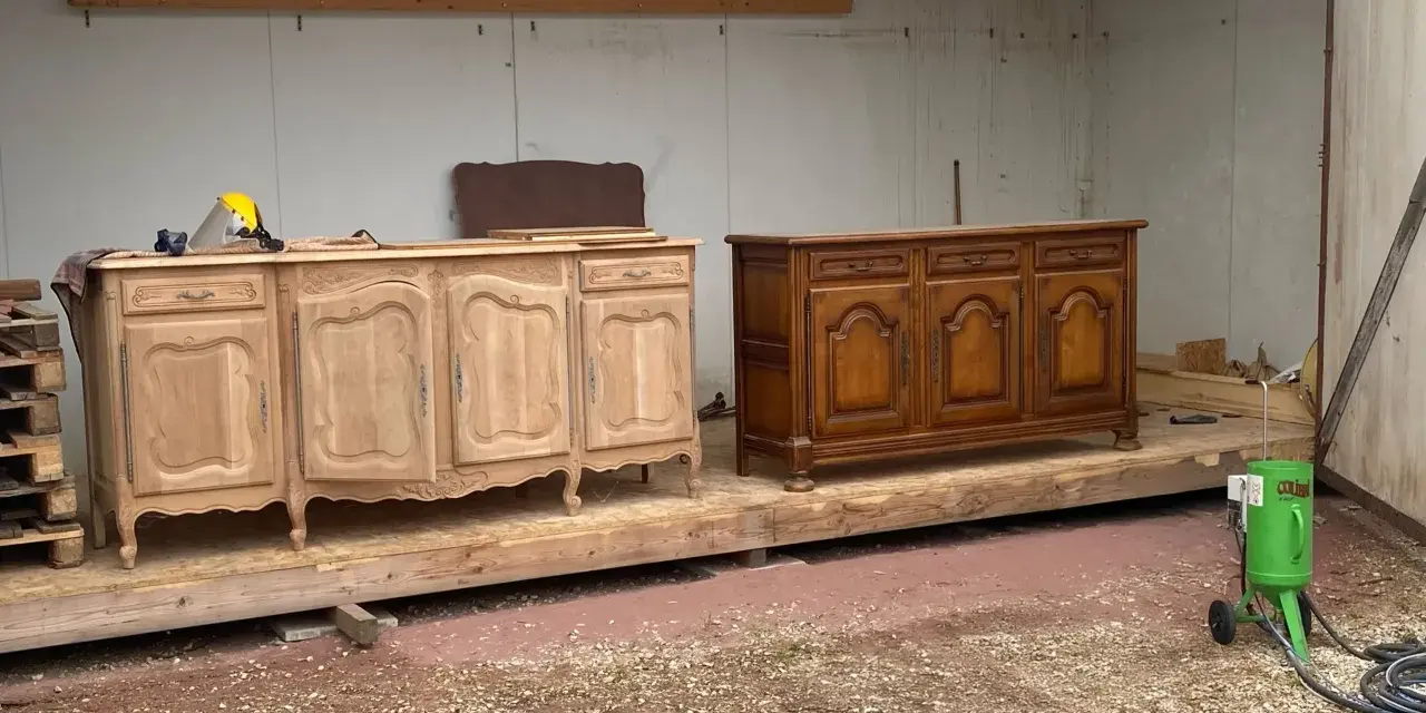 Deux commodes en bois, l'une brute et l'autre vernie, témoignent d'une **réparation meuble en bois**. Un équipement de sablage est prêt à l'emploi.