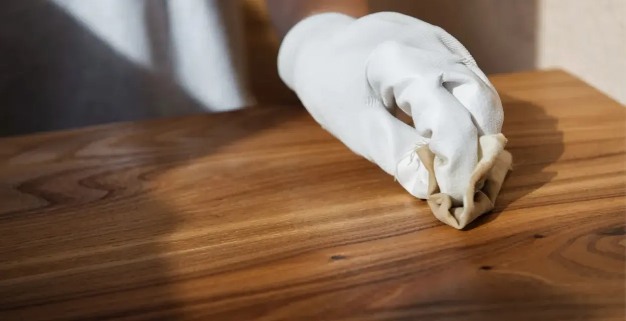 Main d'une personne portant un gant blanc, appliquant de la cire sur un meuble en bois. Apprendre comment cirer un meuble pour le protéger.
