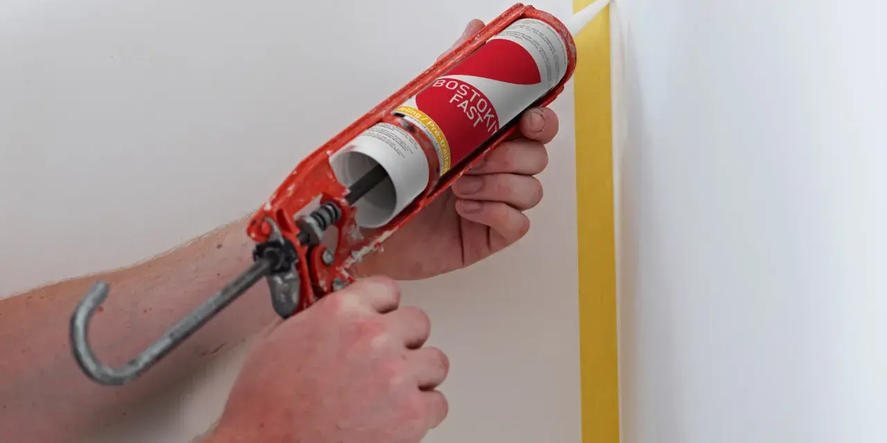 Application de silicone avec un pistolet pour une finition parfaite. Le joint de silicone est appliqué le long d'un coin de mur masqué par du ruban de peintre.