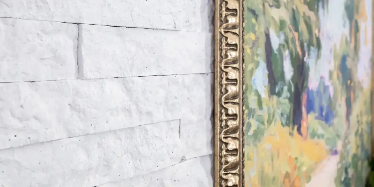 Un mur en pierre peint en blanc sert de toile de fond à un tableau aux couleurs vives, encadré d'or.