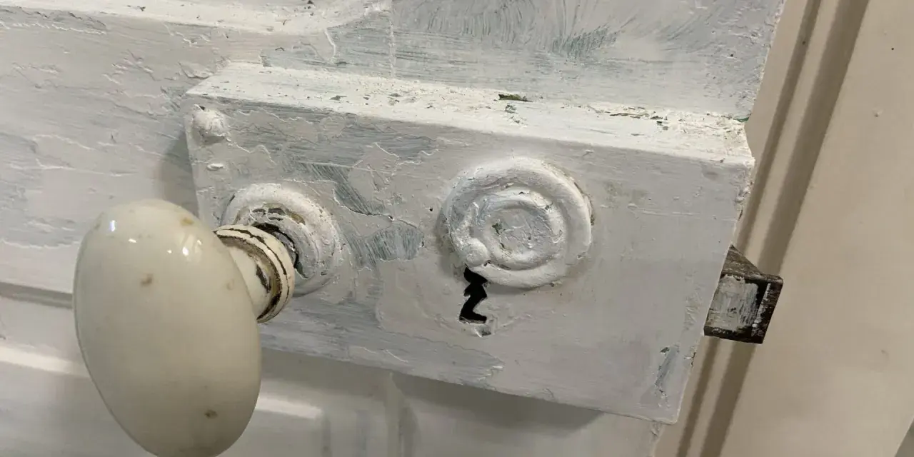 Poignée de porte ancienne et serrure en cours de préparation pour décaper une porte en bois peinte.