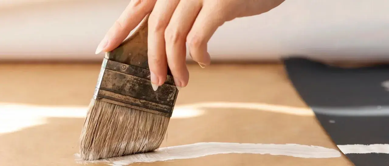 Main d'une personne appliquant une couche de primaire sur du mdf avec un pinceau.