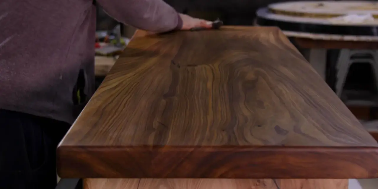 Un artisan polit un meuble en bois de noyer, révélant la beauté du grain. L'essence de térébenthine est utilisée pour faire ressortir la richesse du bois.