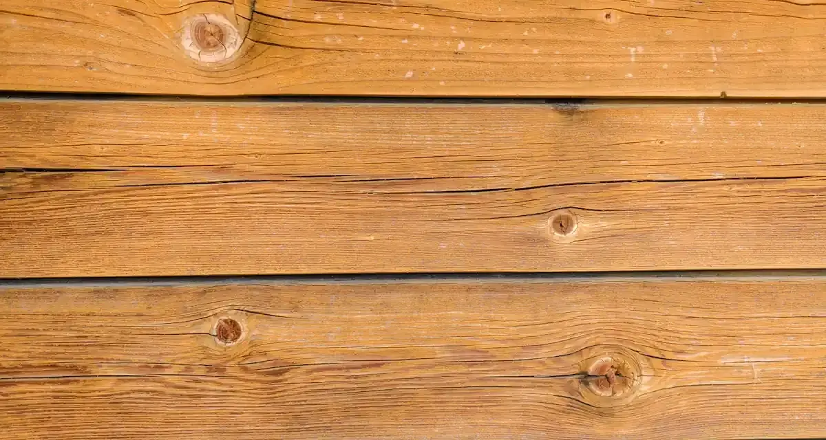Planches de bois brun clair, traitées avec une lasure bois autoclave, révélant des nœuds et des veines naturelles.