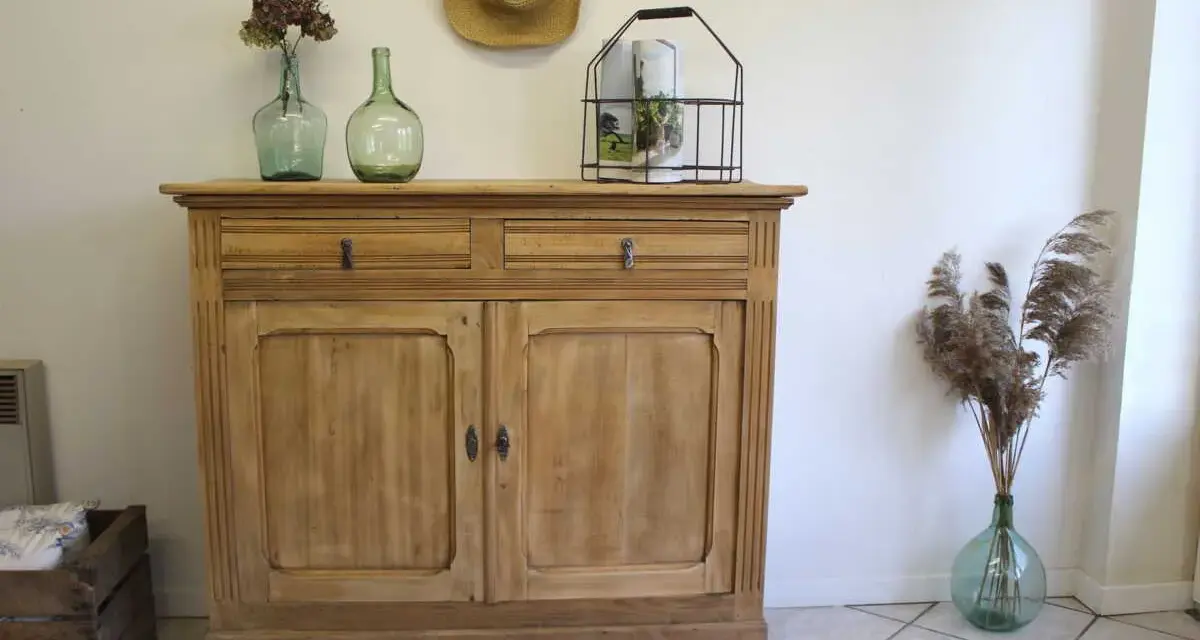 Buffet en bois clair, prêt pour sa restauration. Deux tiroirs et deux portes ornées de moulures. Décoration champêtre avec des vases anciens et des herbes sèches.