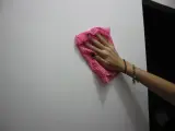 Main tenant une lingette rose pour nettoyer un mur. Une astuce pour savoir comment enlever de la colle forte sur un mur.