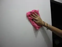 Main tenant une lingette rose pour nettoyer un mur. Une astuce pour savoir comment enlever de la colle forte sur un mur.