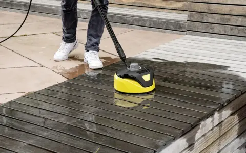 Nettoyage d'une terrasse en bois avec un karcher. L'appareil jaune et noir nettoie le bois sombre, laissant une surface plus claire et humide.