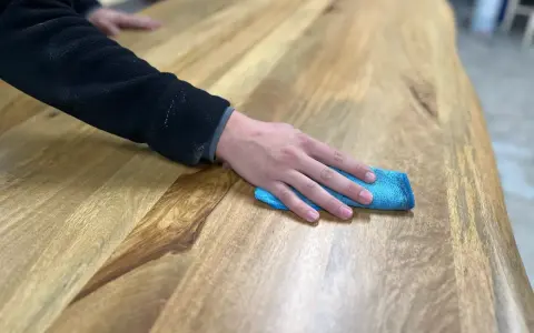 Main d'une personne passant un chiffon bleu sur une table en bois, montrant comment nettoyer une table en bois.