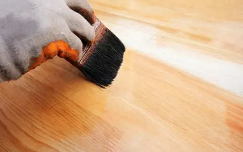 Application d'un vernis protecteur pour le traitement plan de travail bois. La brosse dépose une couche uniforme sur le bois clair.