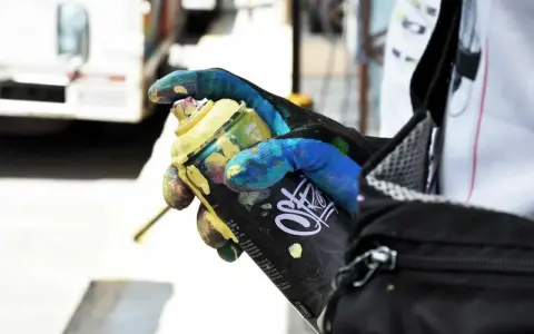 Main tenant une bombe de peinture jaune, un gant coloré montre comment enlever de la bombe de peinture.