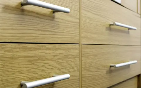 Poignées de tiroirs en aluminium sur des meubles en bois clair. Un guide visuel pour comment fixer un bouton de meuble.