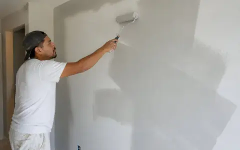 Un peintre applique une couche de peinture grise sur un mur. La question est : peut on enduire sur de la peinture ?