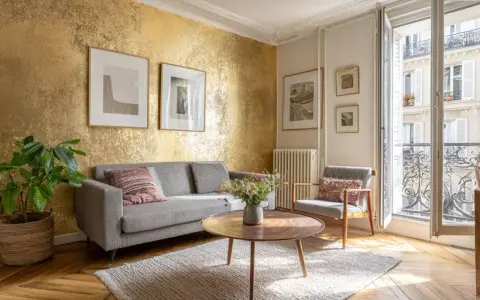 Un salon élégant avec un mur texturé doré, un canapé gris, un fauteuil, une table basse et des tableaux. Une idée pour comment faire du doré avec de la peinture.