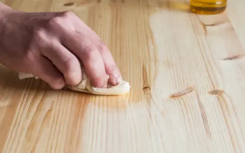 Main d'une personne nettoyant une table en bois avec du vinaigre blanc et un chiffon.