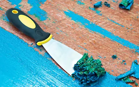 Spatule raclant de la peinture acrylique verte sur une surface en bois bleue écaillée.