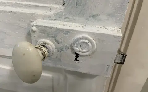 Poignée de porte ancienne recouverte de peinture blanche écaillée, prête à être nettoyée.