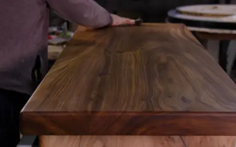 Un artisan polit un meuble en bois de noyer, révélant la beauté du grain. L'essence de térébenthine est utilisée pour faire ressortir la richesse du bois.