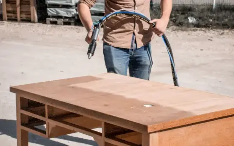 Un homme utilise un appareil pour le décapage chimique bois d'un bureau. La moitié de la surface est déjà propre.