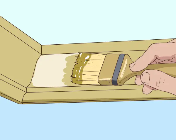 Main tenant pose du mastic sur une moulure en bois avec un pinceau.