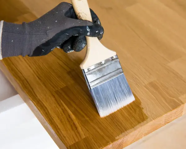 Main tenant enlever huile de lin sur bois avec un pinceau. Le bois est clair et le pinceau applique une couche protectrice.