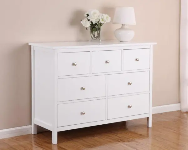 Commode blanche 3 tiroirs, prête à être relookée. Un vase de fleurs et une lampe complètent la scène.