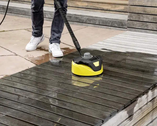Nettoyage d'une terrasse en bois avec un karcher. L'appareil jaune et noir nettoie le bois sombre, laissant une surface plus claire et humide.