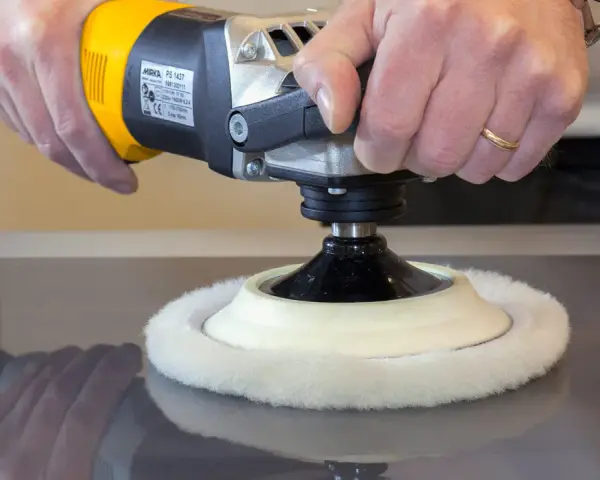 Main d'artisan utilisant une polisseuse pour polir le vernis d'un meuble en bois.
