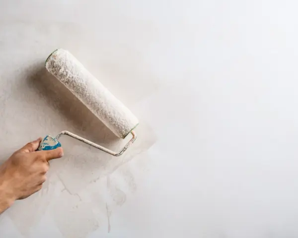 Main d'une personne appliquant une couche de peinture sur un mur déjà peint avec un rouleau.