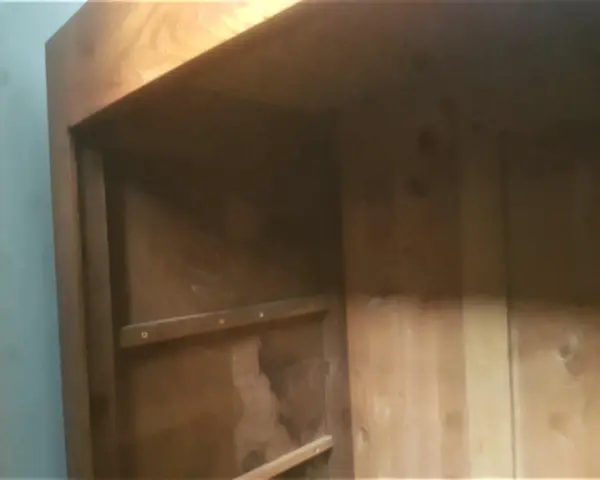 Intérieur d'une armoire ancienne en bois, prête à démonter. Les étagères sont visibles, ainsi que les marques du temps.