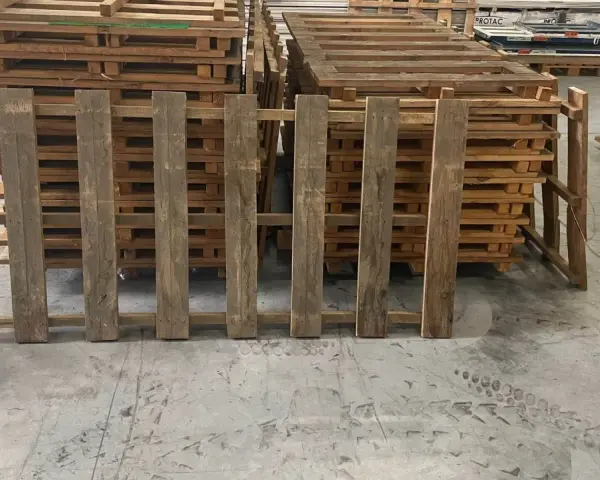 Des planches de bois recycle, issues de palettes, forment une barrière devant d'autres palettes empilées.