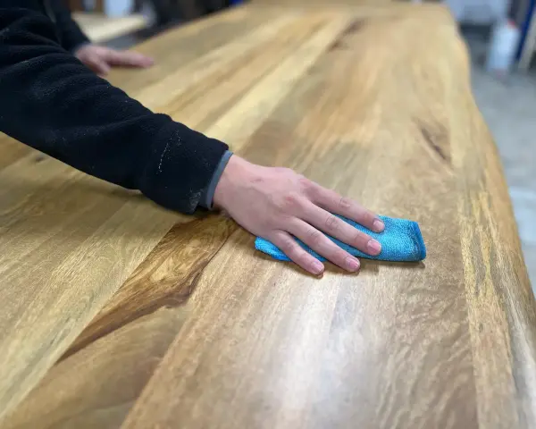 Main d'une personne passant un chiffon bleu sur une table en bois, montrant comment nettoyer une table en bois.