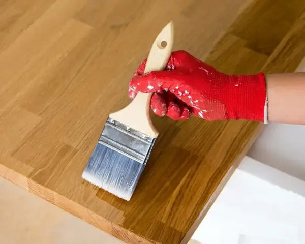 Application d'huile de lin sur un plateau en bois de douglas. La main gantée de rouge applique le produit avec un pinceau.