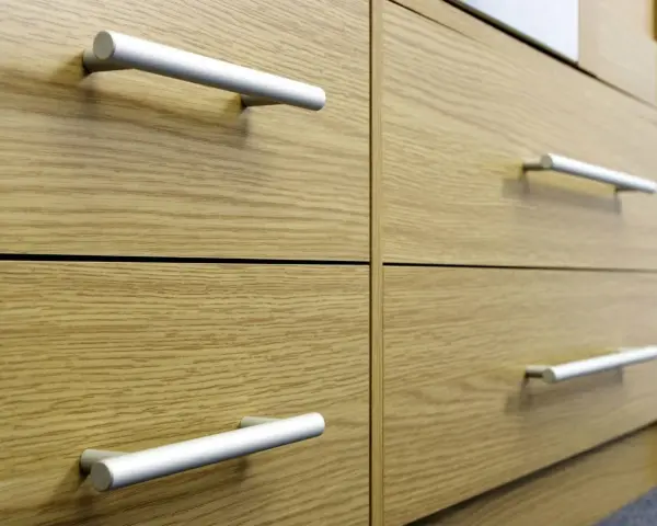 Poignées de tiroirs en aluminium sur des meubles en bois clair. Un guide visuel pour comment fixer un bouton de meuble.