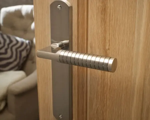 Composition d'une poignée de porte moderne en métal brossé sur une porte en bois clair. Le manche est strié pour une meilleure prise.