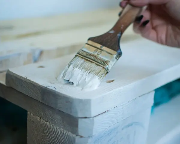 Application de peinture glycéro sur bois brut, sans poncer. La brosse dépose une couche blanche sur la surface.