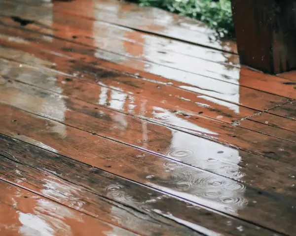 Pluie sur un bois brun, saturateur pas sec, créant des reflets et des ronds dans l'eau.