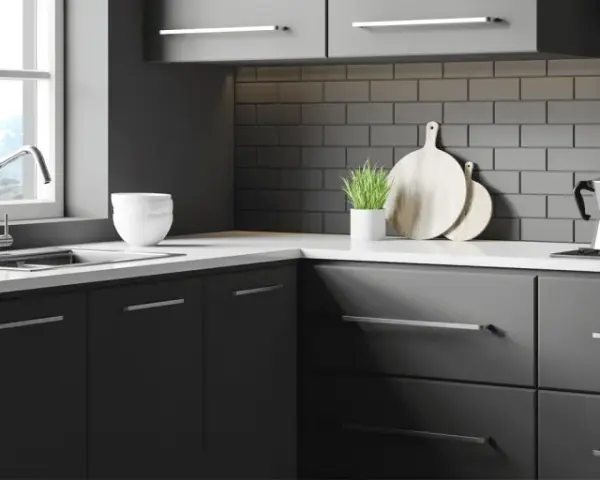 Une cuisine moderne et épurée, idéale pour rénover sa cuisine sans changer les meubles. Des placards sombres, un plan de travail blanc et un crédence en briques grises.