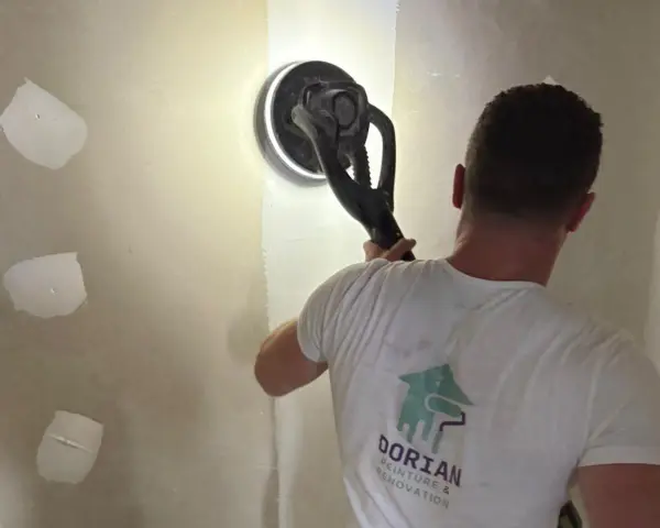 Un ouvrier utilise une ponceuse girafe pour poncer un mur en plâtre, préparant la surface pour la peinture.