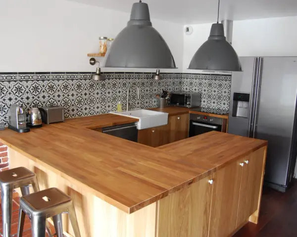 Cuisine moderne avec îlot central en bois, carrelage mural graphique et tabourets industriels. On dirait qu'on a réussi à faire une cuisine avec des vieux meubles revisités.