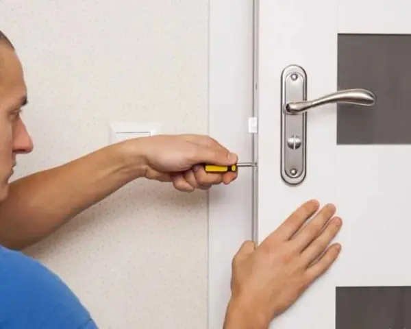 Un homme utilise un tournevis pour installer une serrure sur une porte de chambre.