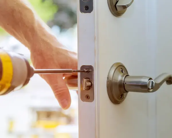 Main tenant répare une serrure cassée sur une porte fermée. Un tournevis est utilisé pour fixer le mécanisme.
