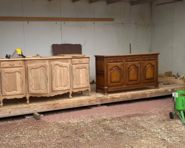 Deux commodes en bois, l'une brute et l'autre vernie, témoignent d'une **réparation meuble en bois**. Un équipement de sablage est prêt à l'emploi.