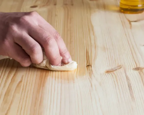 Main d'une personne nettoyant une table en bois avec du vinaigre blanc et un chiffon.