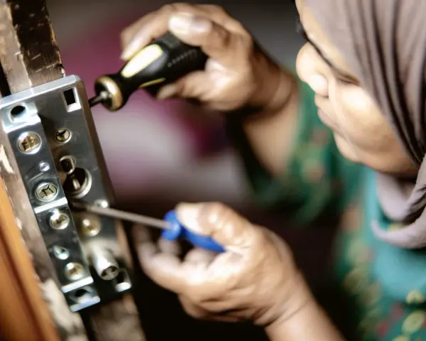 Une personne en hijab utilise un tournevis pour enlever vieux gonds d'une porte en bois.