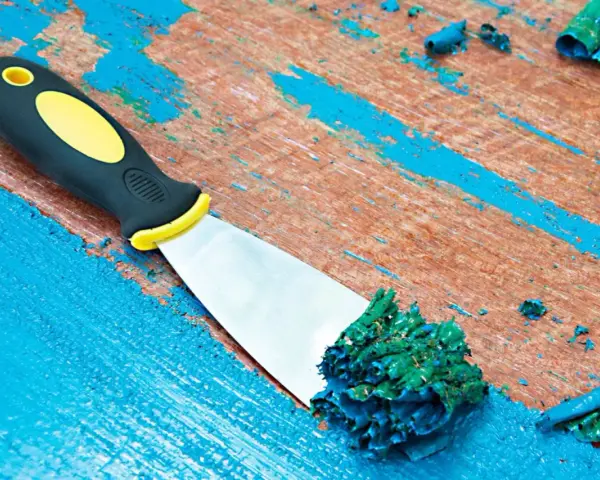 Spatule raclant de la peinture acrylique verte sur une surface en bois bleue écaillée.