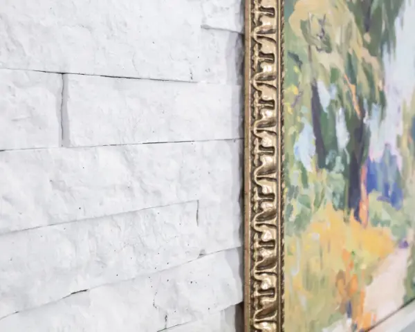 Un mur en pierre peint en blanc sert de toile de fond à un tableau aux couleurs vives, encadré d'or.