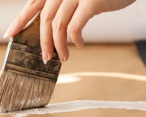 Main d'une personne appliquant une couche de primaire sur du mdf avec un pinceau.