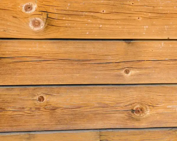 Planches de bois brun clair, traitées avec une lasure bois autoclave, révélant des nœuds et des veines naturelles.