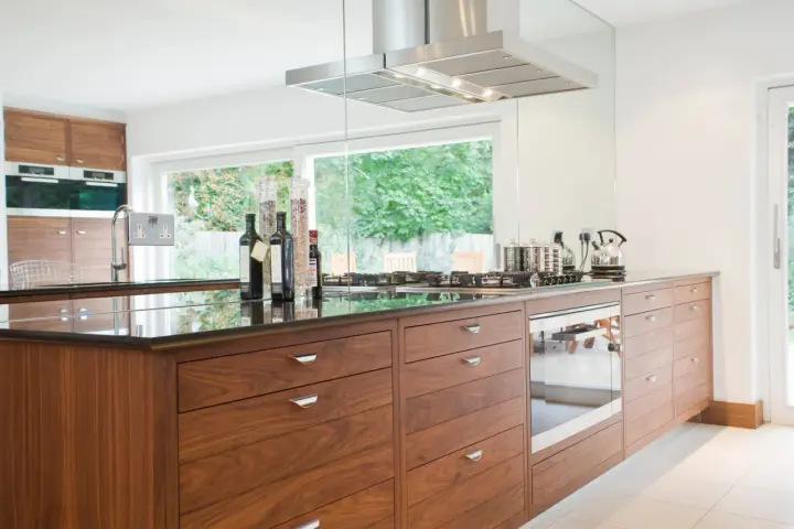 Cuisine moderne avec îlot central en bois, plan de travail en granit noir, et électroménagers intégrés. Une rénovation cuisine bois réussie.